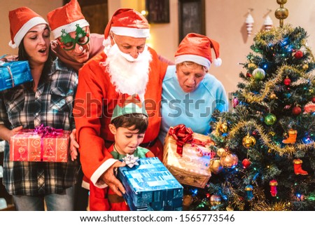 Multi generation family having fun at christmas night giving each other x mas presents - Winter holiday concept with parents and children opening gifts together - Focus on grandpa and nephew face