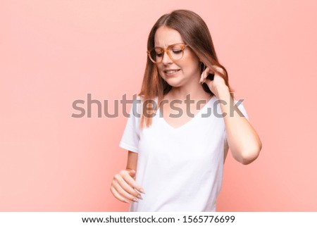 young red head woman feeling stressed, frustrated and tired, rubbing painful neck, with a worried, troubled look against flat wall