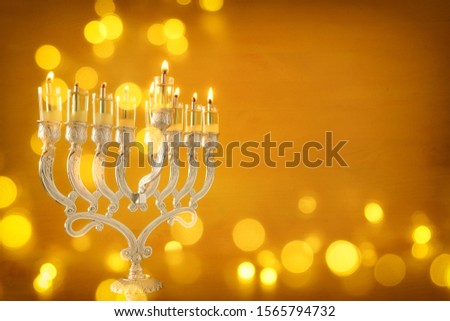 Religion image of jewish holiday Hanukkah  with menorah (traditional candelabra) and oil candles over yellow background