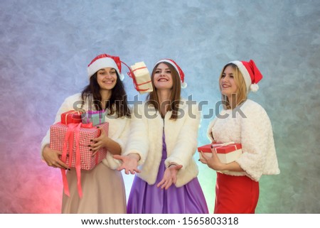 Three happy girls throwing up their gift boxes. They are in elegant dresses and fur jackets
