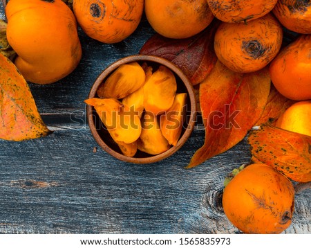 Top view on ripe orange persimmons, autumn leaves and a wooden cup lie on the surface of a wooden table. View from above.