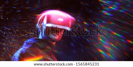 Young man on virtual reality background. Guy using VR helmet. Augmented reality, future technology, game concept. Pink neon light, rainbow flares.
