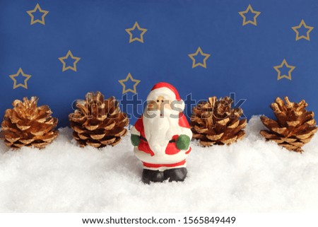 santa claus or saint nicholas standing in snow in front of gold colored pine cones and a dark blue starry sky 