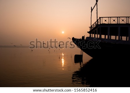 Sunrise on the river Ganges in Varanasi, India. Fog, seagulls and boat silhouettes.