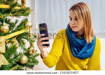 Woman female sitting at home in front of the christmas tree taking photos selfies using smart mobile phone video chat family