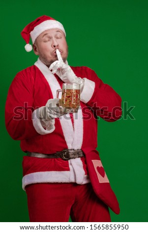Emotional male actor in a costume of Santa Claus holds a glass of beer in his hands and poses on a green chrome background
