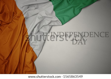 waving colorful national flag of cote divoire on a gray background with text independence day. concept