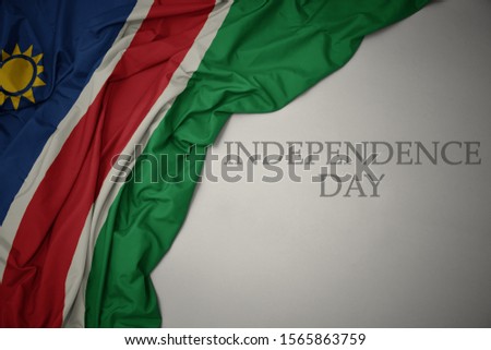 waving colorful national flag of namibia on a gray background with text independence day. concept