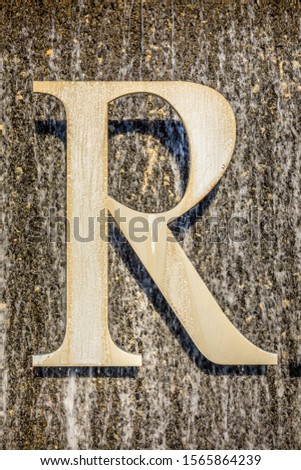 Letter R made of metal attached on a marble water with running water