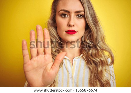 Young beautiful woman wearing stripes shirt standing over yellow isolated background with open hand doing stop sign with serious and confident expression, defense gesture