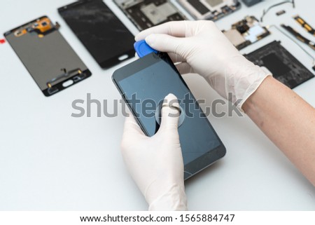 Cropped view of repairman in gloves using special instrument, changing damaged screen and showing process of mobile phone repair in service center