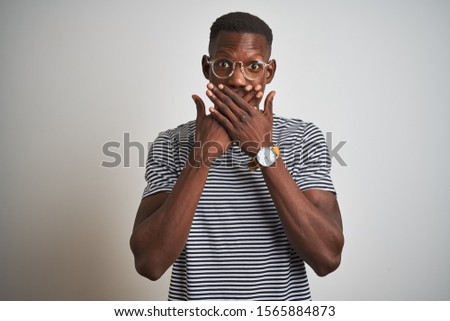 African american man wearing striped t-shirt and glasses over isolated white background shocked covering mouth with hands for mistake. Secret concept.