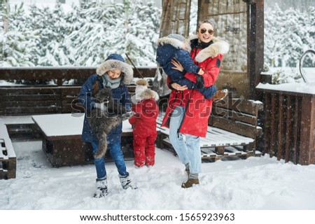 A young mother with her tree children have a fun and playing snowballs outdoor near the home