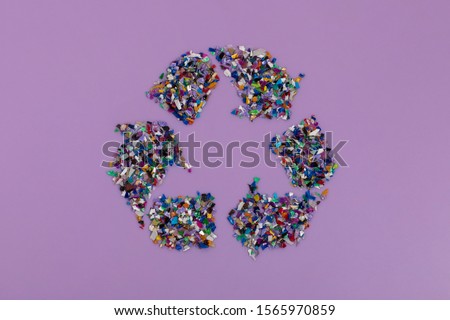 Recycle symbol consisting of small plastic pellets collected from the sea water. Rethinking the environment by reducing or reusing plastics. Circular economy concept. Lilac purple background
