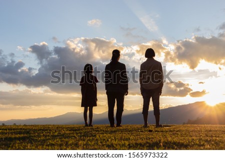 Group of children and woman stands on mountain top and looks at sunset. 