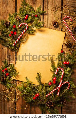 Christmas wooden background - vintage sheet of paper with decorations around (pine branches, candy canes). Rustic layout with free copy (text) space. Captured from above (top view, flat lay).