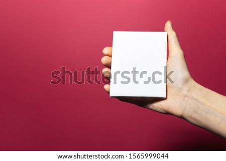 Close-up of female hand holding white paper with mockup on background of pink coral color.