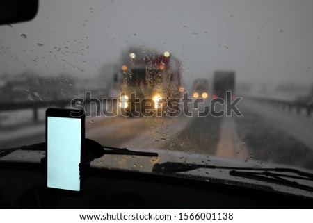 Smartphone in car. Driving a car with smartphone in holder. Mobile phone with isolated white screen. Blank empty screen. Copy space. Empty space for text. rainy evening. night scene. 