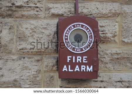 An old vintage brown fire alarm on stone brick wall.