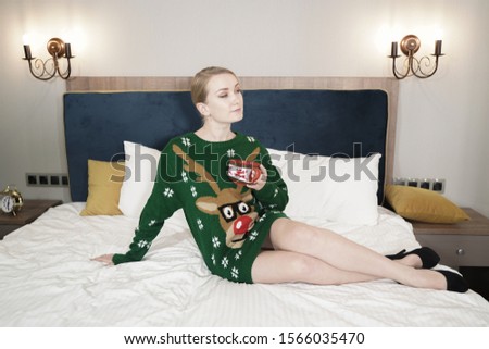 Happy young Caucasian pretty girl wearing Santa sweater and enjoys in the bedroom alone