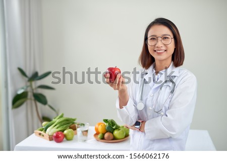 Nutritionist desk with healthy fruits, juice and measuring tape. Dietitian working on diet plan at office, smiling at camera. Weight loss and right nutrition concept Royalty-Free Stock Photo #1566062176