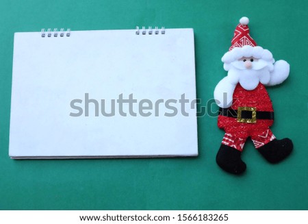 copy space and top view Santa Claus and white notebook on green background. concept Christmas and happy new year