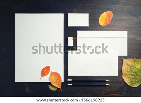 Photo of blank stationery set and autumn leaves on wooden background. Corporate stationery template. Flat lay.