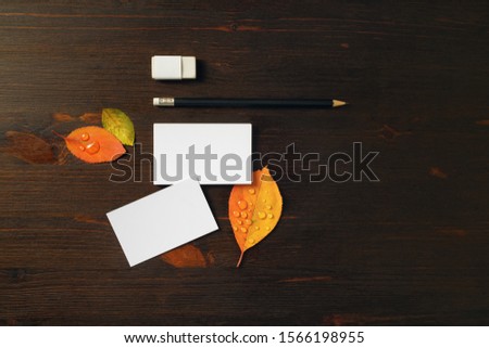 Photo of white business cards, pencil, eraser and bright autumn leaves on wooden background. Blank stationery template for placing your design.