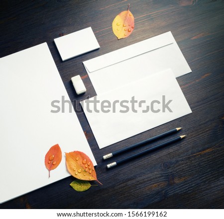 Photo of blank branding stationery set and autumn leaves on wood table background.
