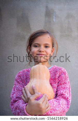 Young little girl holds autumn pumpkin squash. 