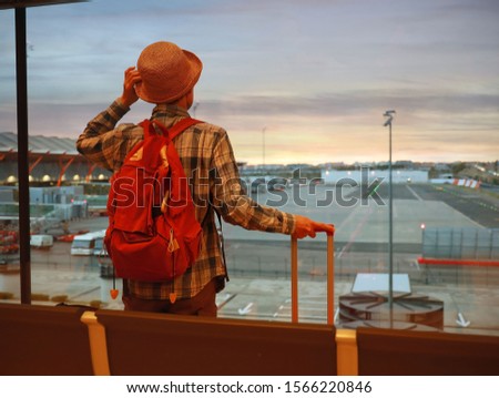 Back view of young  backpacker man  and a luggage which looking the airplane on the window  at a terminal airport