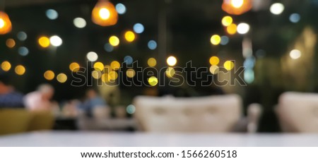 Blurred white table and chair inside restaurant for dinner with bokeh yellow and blue light effect. 