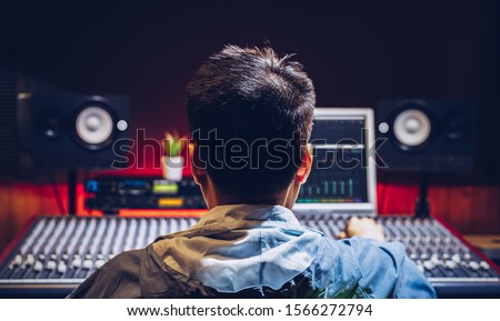 back of asian male music producer working on audio mixing console in recording studio. music production, broadcasting, post production concept