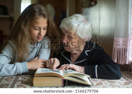Cute teen girl with her old great-grandmother reading a book. Royalty-Free Stock Photo #1566279706