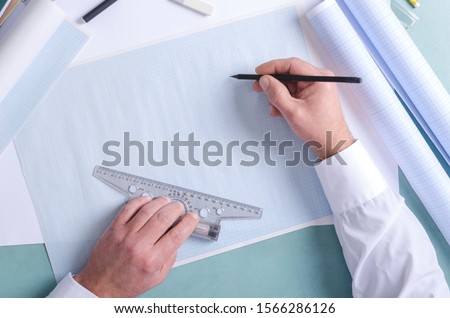 Top view of constuctor`s hands who using t-square and pencil. Draftsman at work, drafting on the graph paper. Free space for design