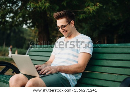 Side view portrait of a young confident freelancer working outdoor in the park on his laptop smiling.