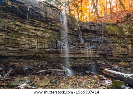 Late Autumn Scene featuring rocky cascade waterfalls, snow covered ground, fall colors trees and low water flow