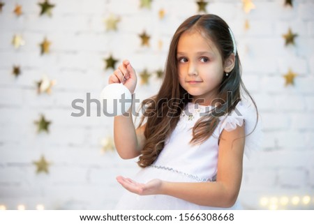 A beautiful child with a Christmas ball. Girl in a white dress with a Christmas toy.