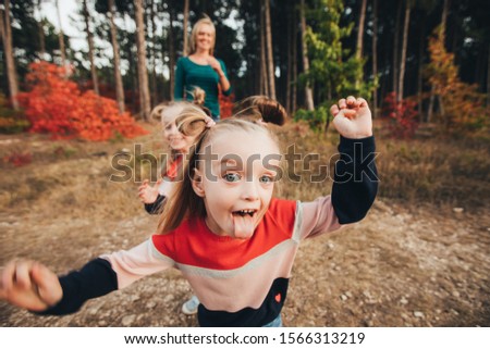 Blonde mother and her twin daughters are walking in the autumn forest among red trees.