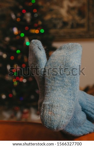 Two legs in blue wool socks lie on a leather sofa. Decorated Christmas tree in the background
