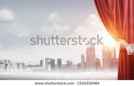 Human hand opens red velvet curtain to modern cityscape and cloudy sky