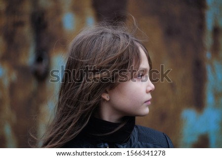 serious young girl in a black leather jacket against a rusty wall