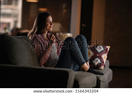 Beautiful woman watching movie in the night sitting on a couch in the living room at home Royalty-Free Stock Photo #1566343204