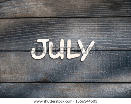 The name of the month is composed of light wooden letters on dark wood. The month of July. 