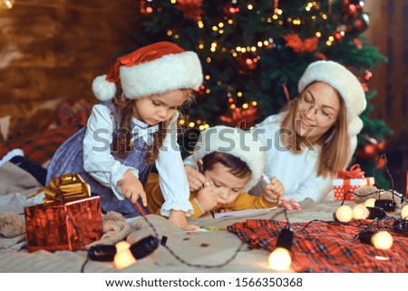 Mom with children draws in the room with the Christmas tree.