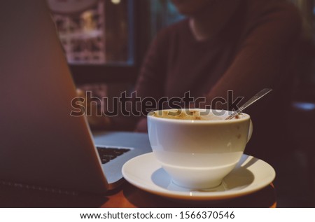A young girl working with a cup of cappuccino coffee with laptop white screen on table. Royalty high quality free stock photo image of a woman typing, working on laptop with coffee cup in coffee shop