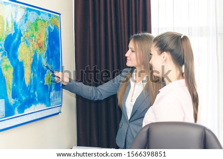 Two business-like young women plot a route on a geographical map for the delivery of cargo. International logistics and cooperation. Royalty-Free Stock Photo #1566398851