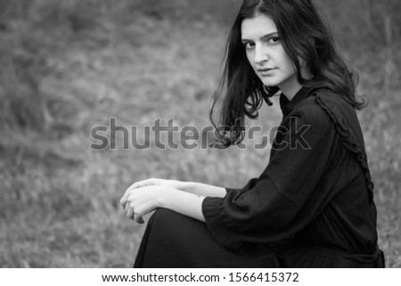 Young fairytale girl Cinderella in vintage black dress on a background of countryside, dry grass hills and trees. Natural without strong makeup. Photo with film noise. Black and white photography