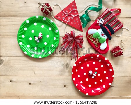 Blurry green & red polka dot paper plates with red ribbon and Christmas ornament accessories on wooden background.The concept of X'mas party, celebration,decoration.Copy space with Selective focus.