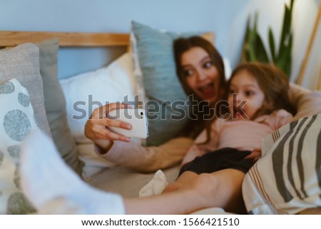 mom and daughter grumble in bed and take pictures of themselves on the phone